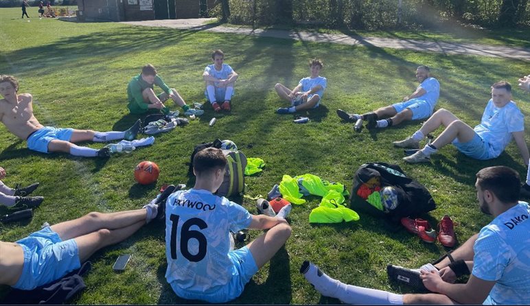 BSMS men's football team sitting down in a circle on the grass