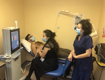 A clinician named Sumita Verma carrying out a fibroscan on a patient with a nurse, looking at a computer screen in a yellow room