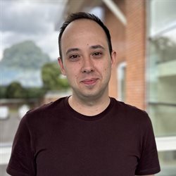 A head and shoulders photo of Dr Fabio Simoes in a purple t shirt next to the medical research building on campus at the BSMS